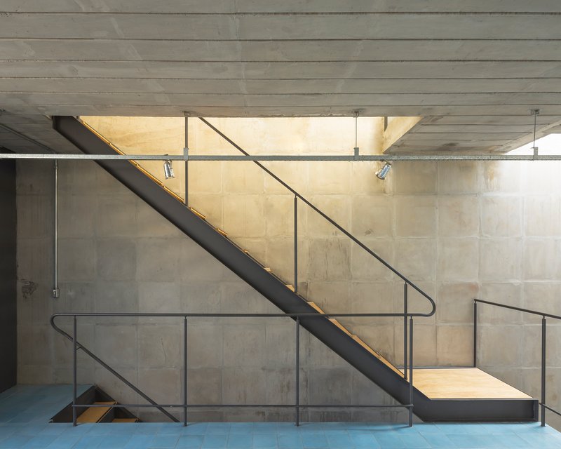 Steel staircase with tubular handrails and brass LED strip lighting against board-formed concrete walls