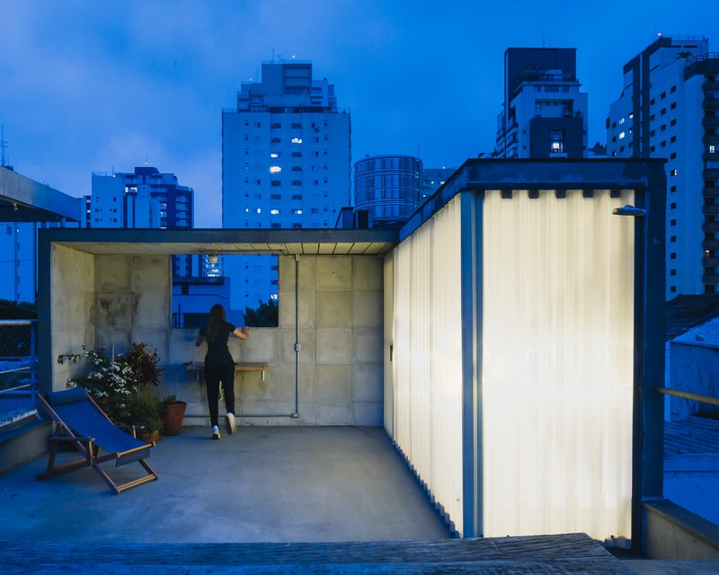 Rooftop terrace with translucent corrugated walls and glass pavilion at dusk with city skyline beyond
