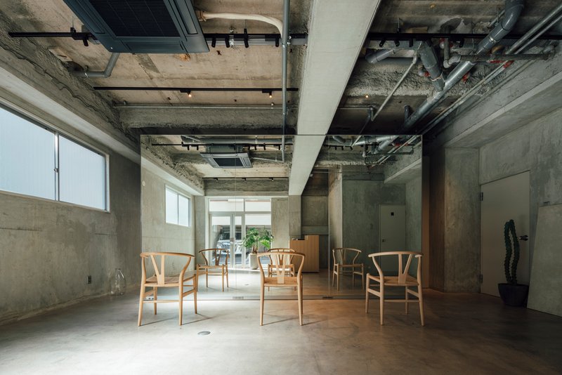 Interior with exposed concrete ceiling and mechanical systems above wooden chairs on polished floor