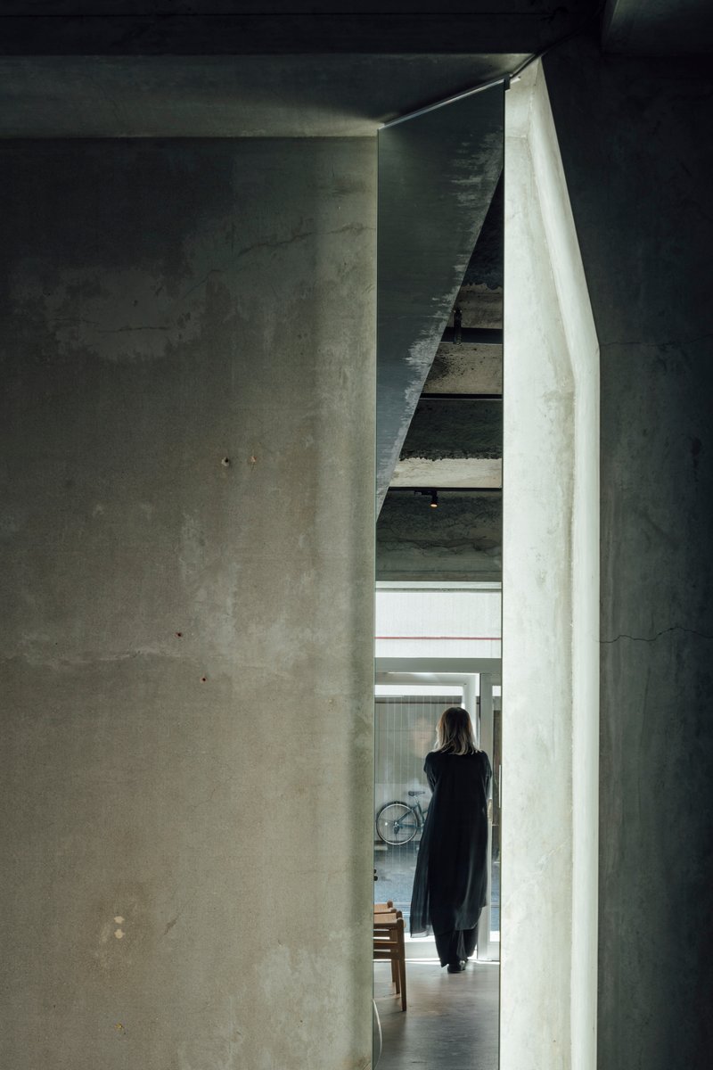 Narrow concrete passageway with a figure walking toward a staircase under indirect natural light