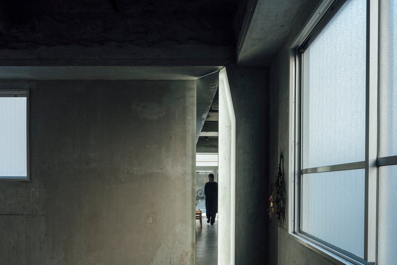 Concrete corridor with a figure visible through an angled doorway beneath a dark painted ceiling