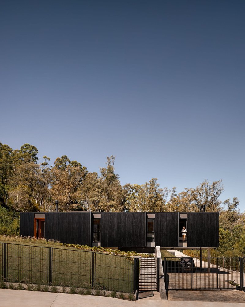 Elevated blackened wood facade with mesh fencing and concrete ramp under clear afternoon sky