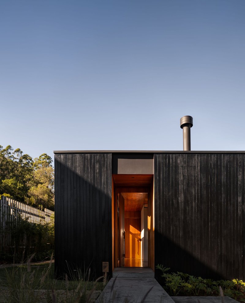 Front entry with vertical timber cladding and a warmly lit threshold at twilight