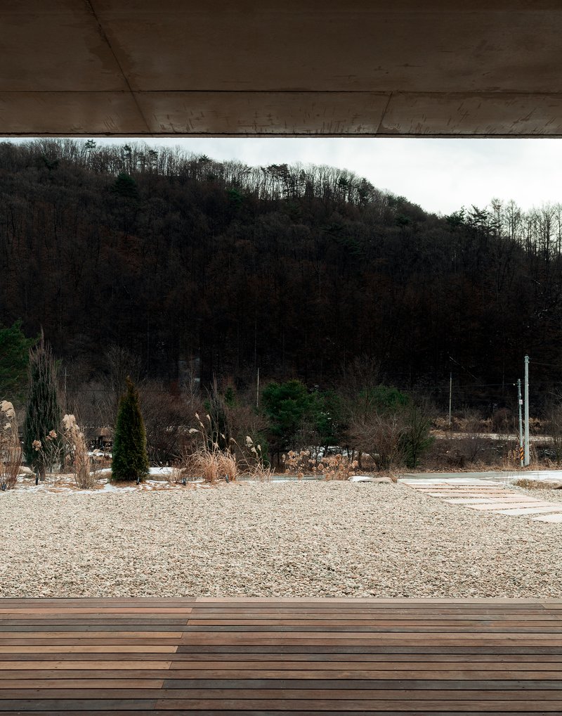 View from beneath the concrete roof slab toward the forested hillside beyond the gravel terrace