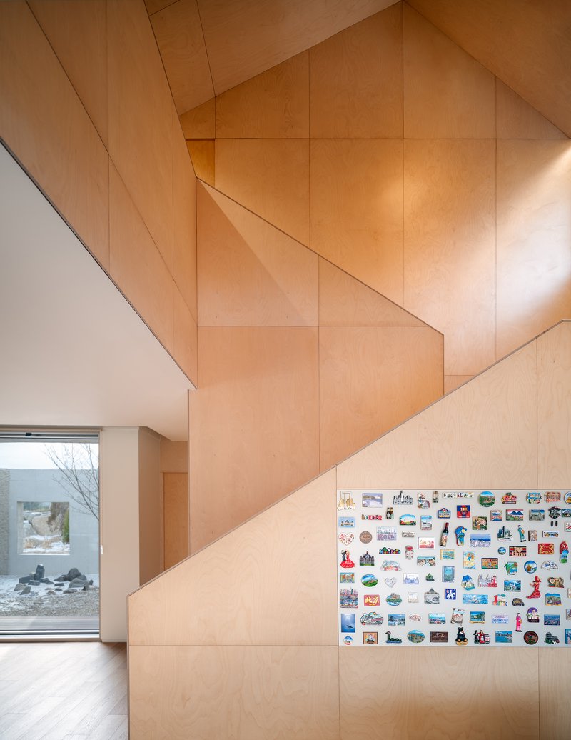 Plywood-paneled stairwell wall with triangular gable geometry and sticker collection below tall window