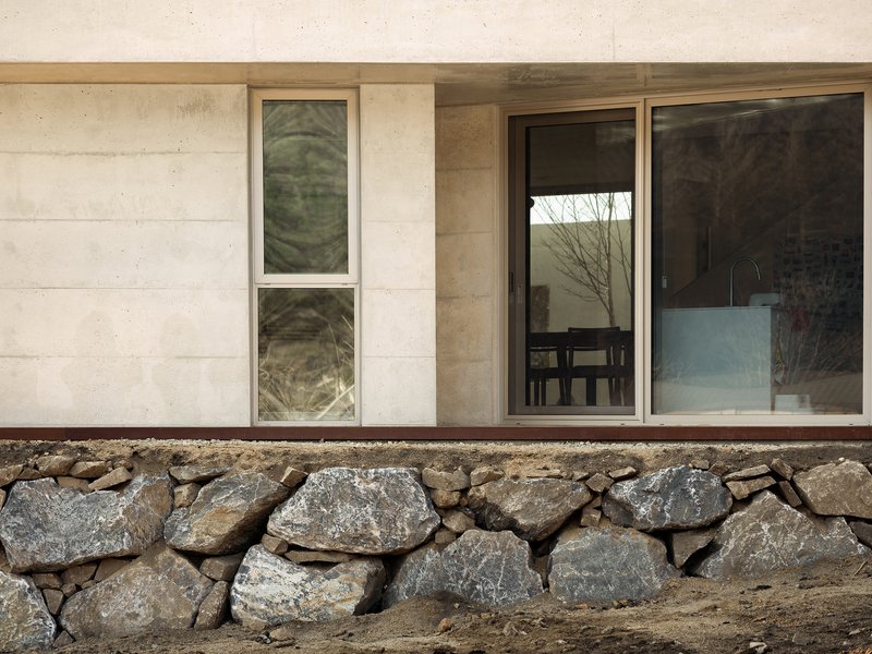 Concrete facade with timber window and sliding glass door above a fieldstone retaining wall