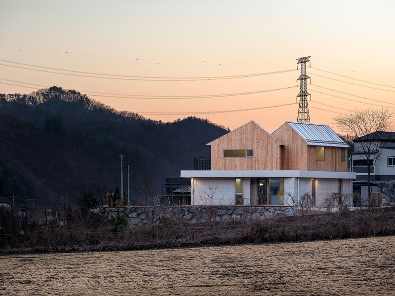 Two-storey residence with timber-clad gabled volumes atop a concrete base at dusk