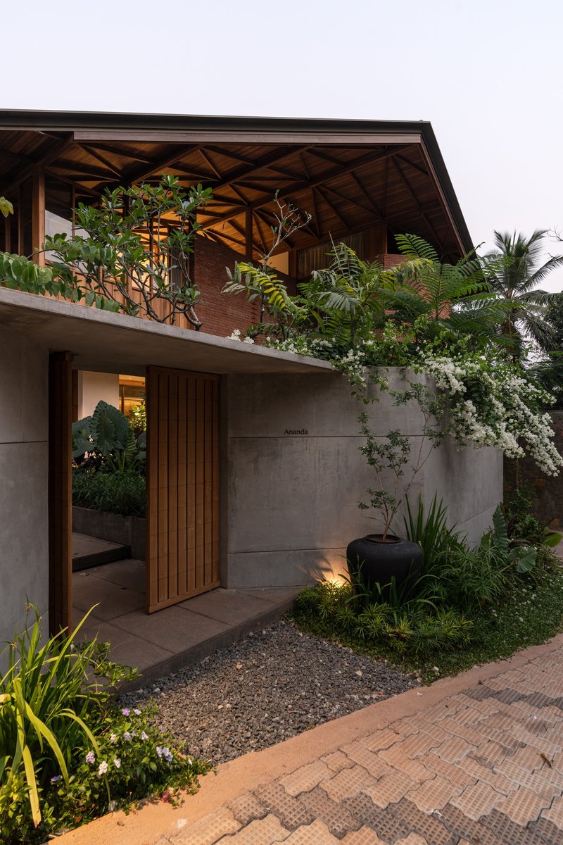 Concrete entrance wall with timber slat door and planted terrace balcony above at dusk
