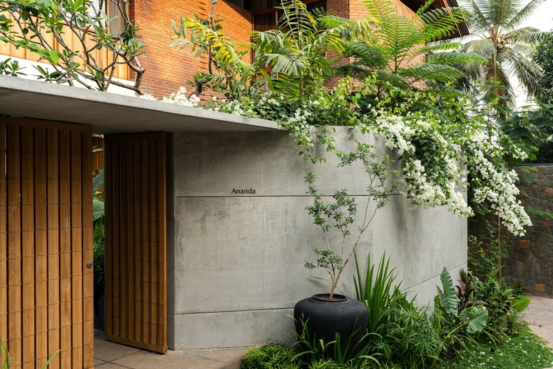 Entrance wall in concrete panels with timber slatted doors and flowering vines cascading from rooftop planter