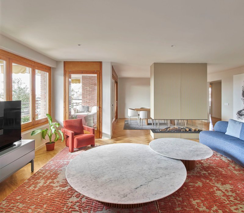 Living room with vertically fluted fireplace wall, marble coffee tables, and timber-framed windows overlooking greenery