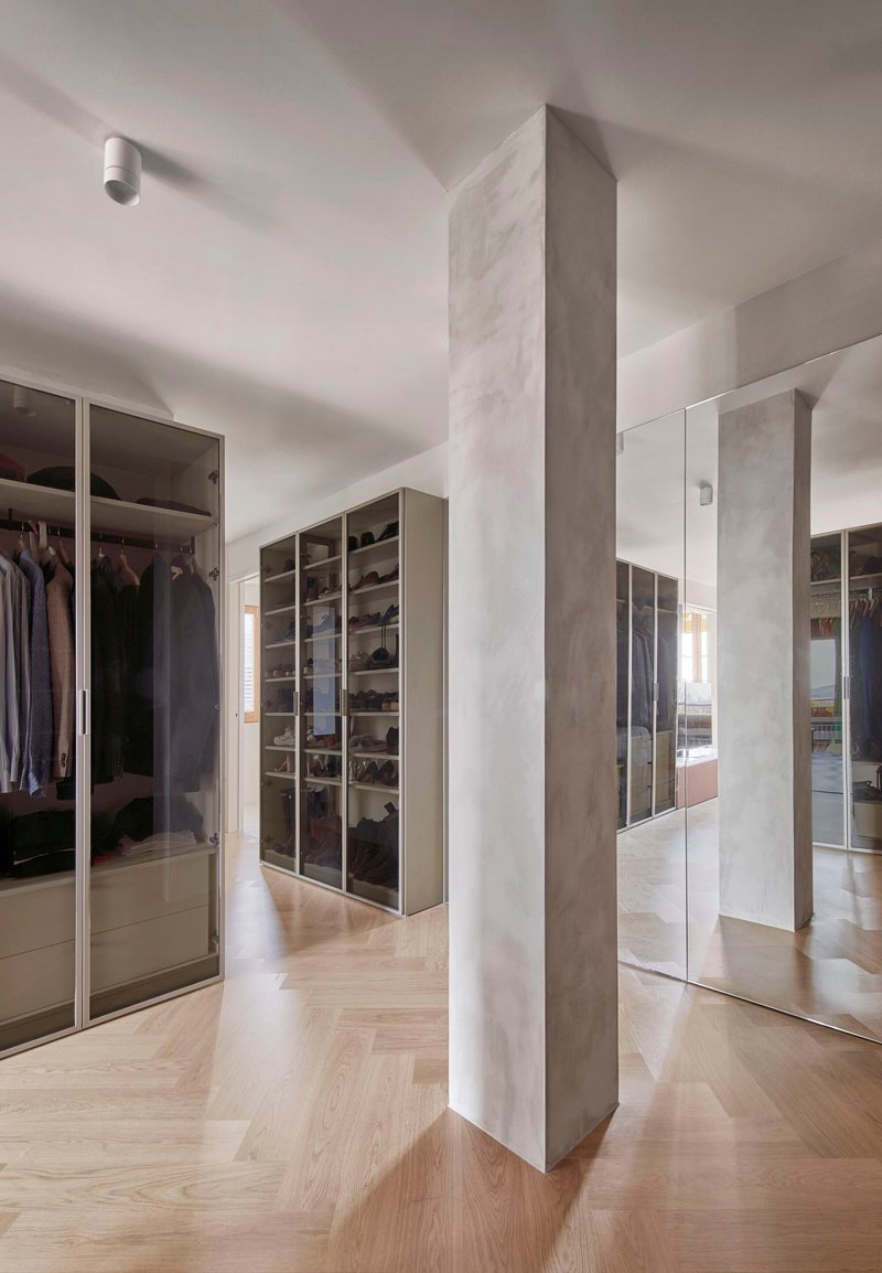 Dressing room with mirrored wardrobes and freestanding terrazzo-clad column on herringbone oak flooring