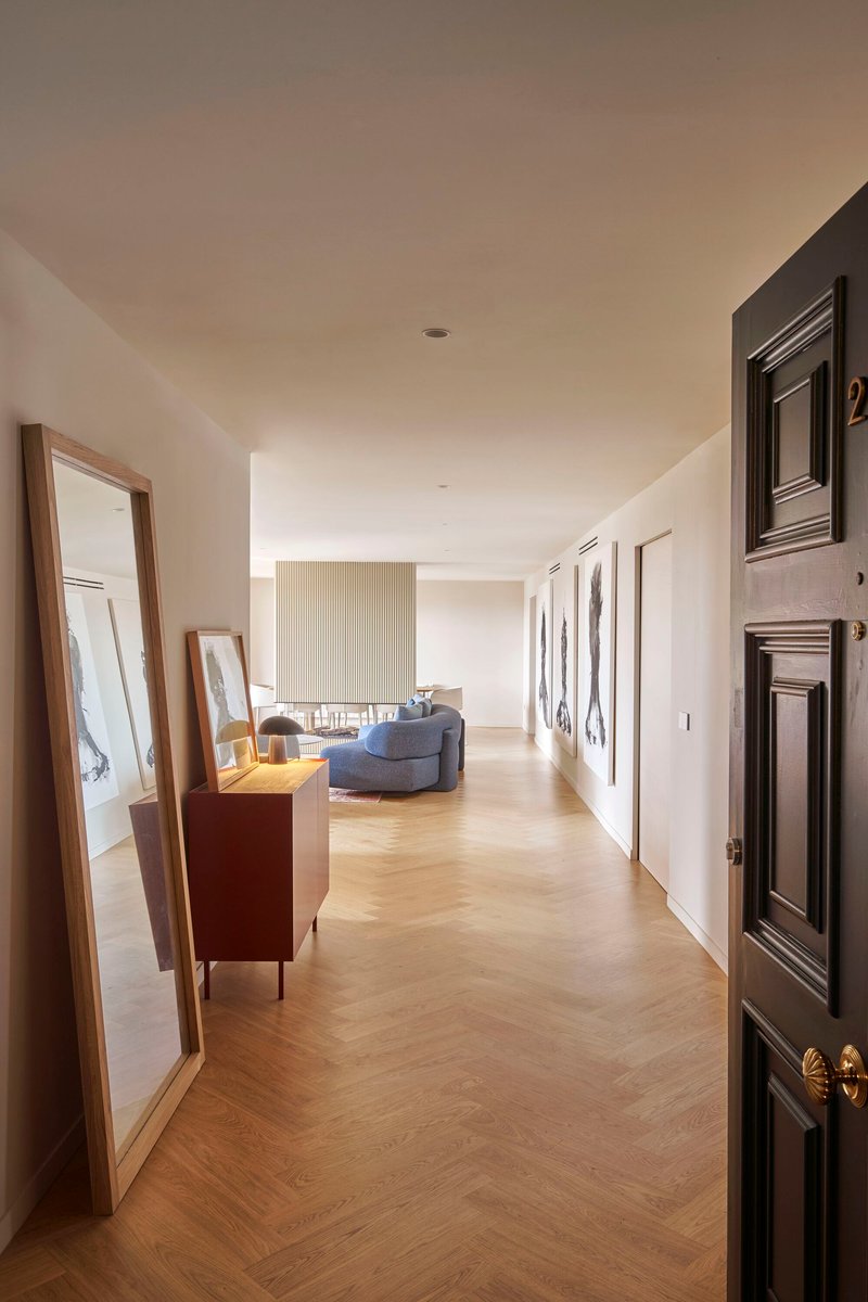 Long hallway with chevron parquet flooring and framed artwork leading to a seating area