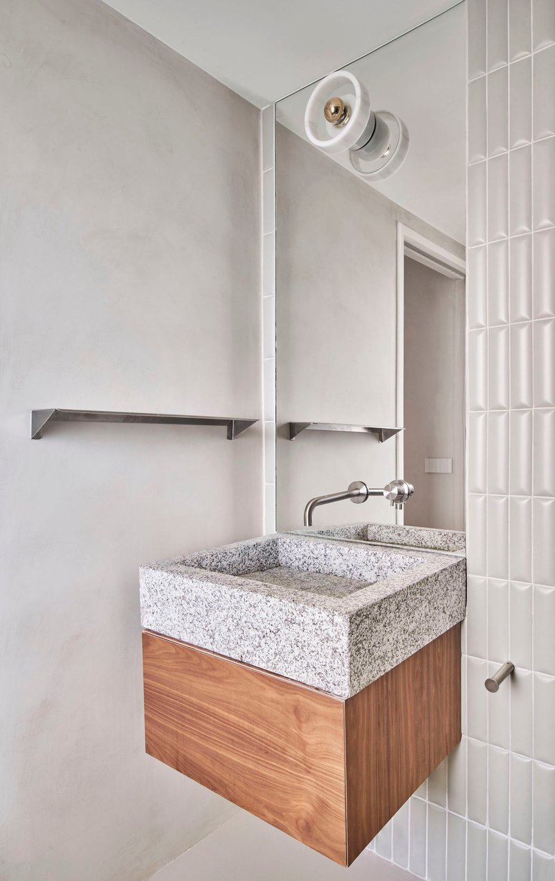 Bathroom vanity with terrazzo sink on timber cabinet beside vertical white tile wall