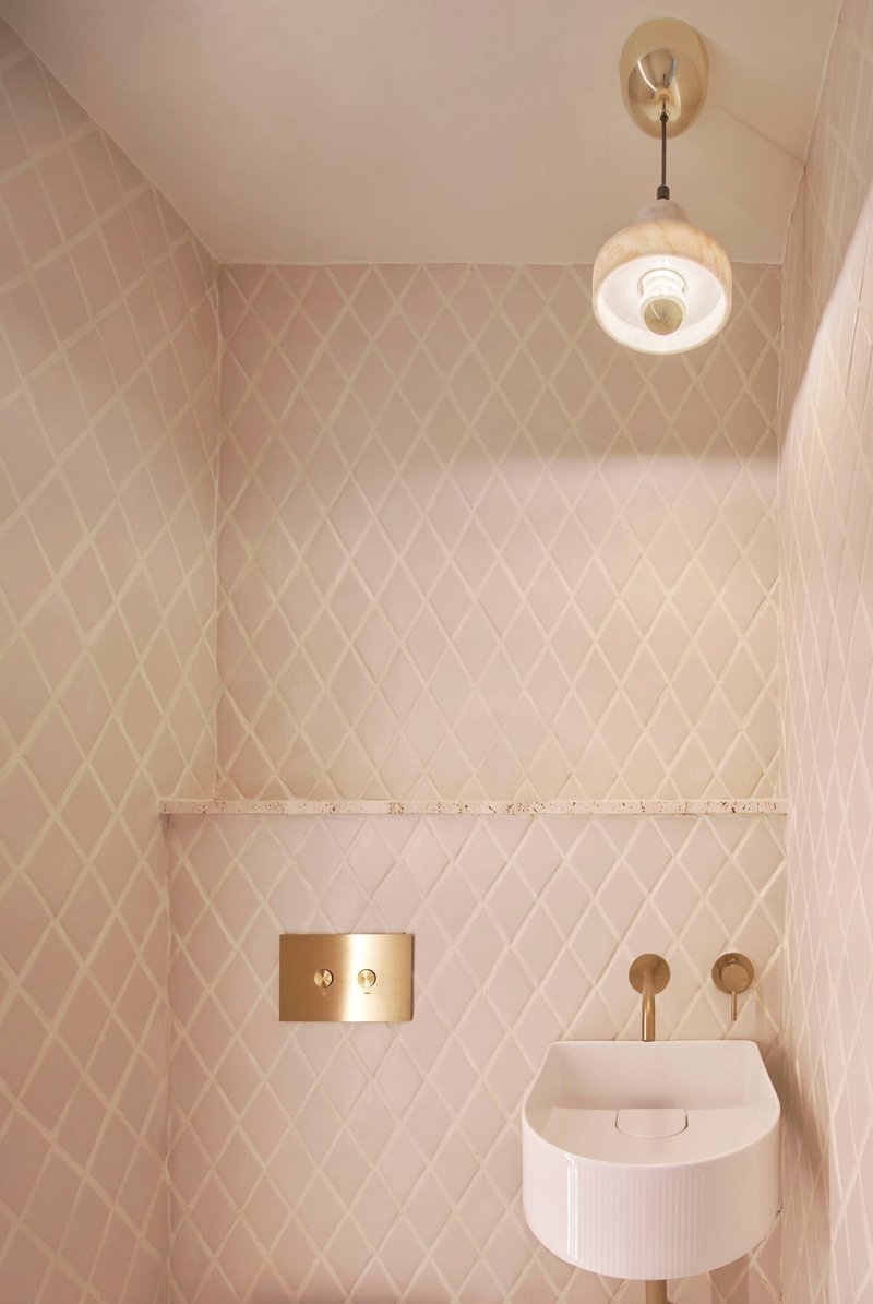 Compact bathroom with diamond-pattern tile walls, brass fixtures, and ribbed wall-mounted sink below pendant light