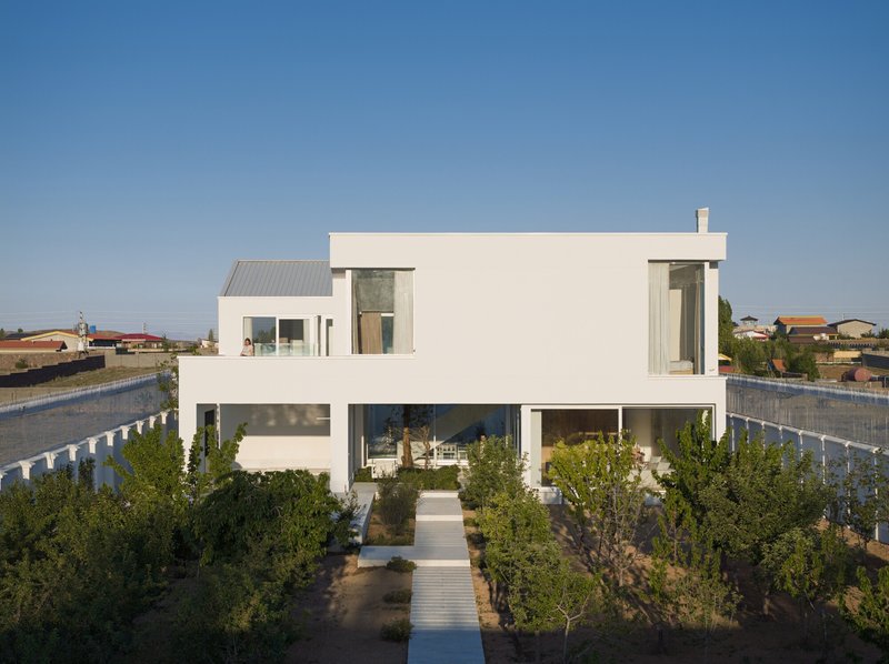 White rendered facade with recessed balcony and planted garden with olive trees under clear sky