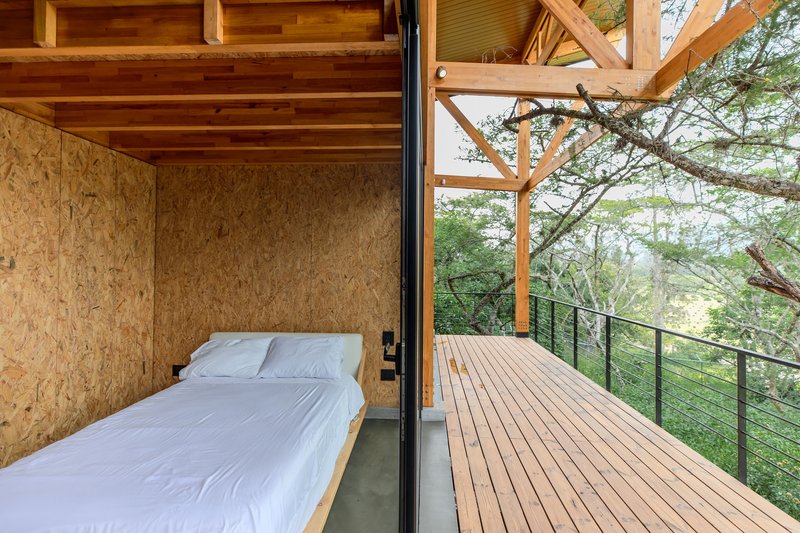 Bedroom with oriented strand board walls opening onto a timber deck with cable railing under morning light