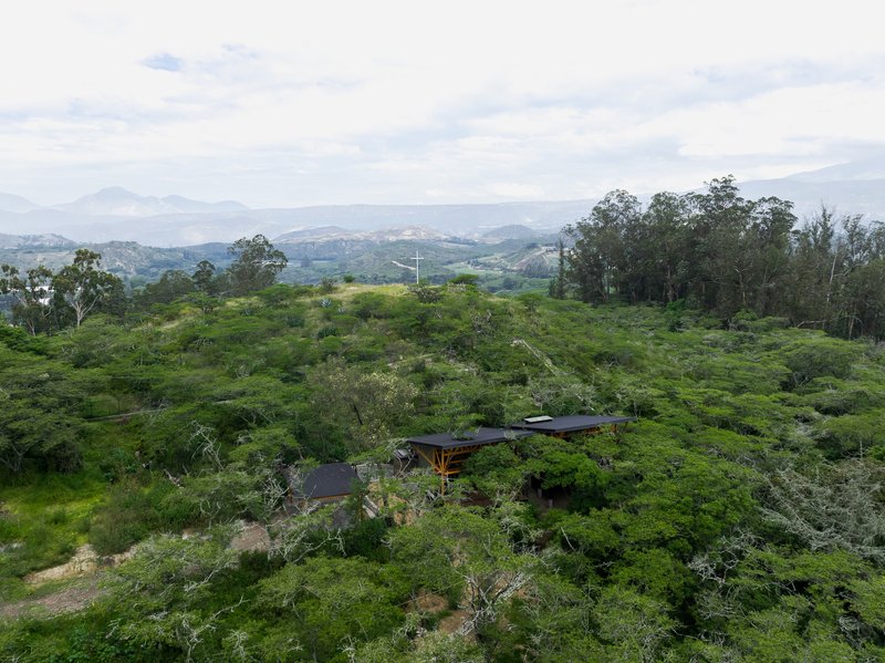 Aerial view of low-slung volumes nestled within hillside vegetation under overcast mountain sky