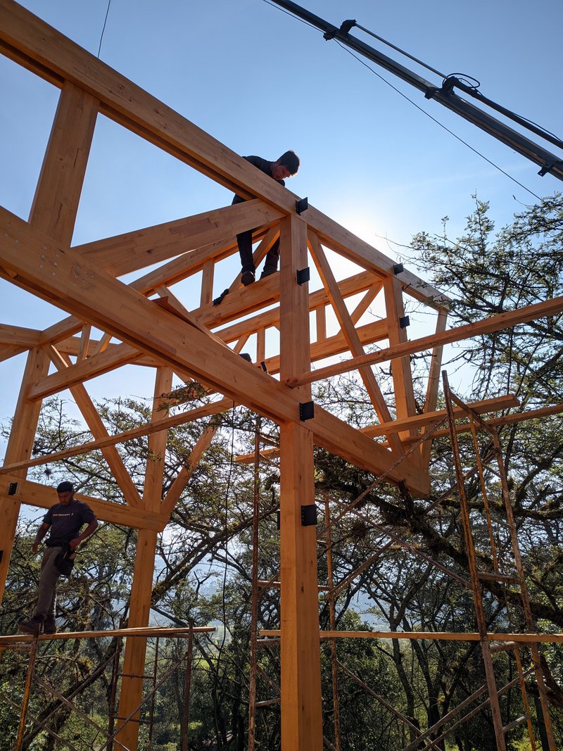 Workers assembling timber frame structure with steel connectors under a clear blue sky