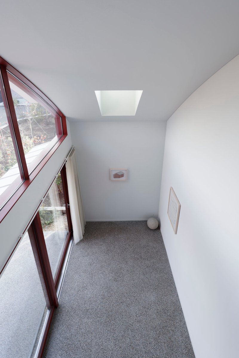 Narrow hallway with angled glazing, terrazzo flooring, white walls and central skylight above