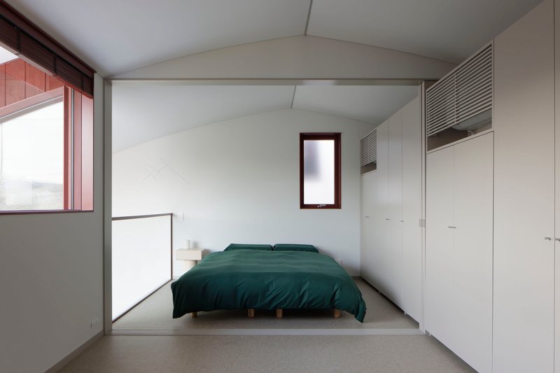 Bedroom with vaulted ceiling, built-in wardrobes and narrow vertical window framing distant view