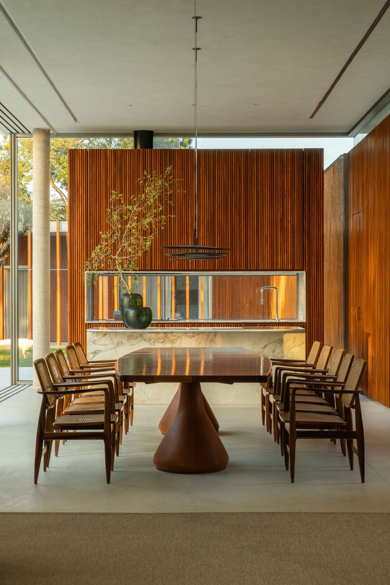 Dining room with sculptural timber table beneath vertical wood slat walls and clerestory windows