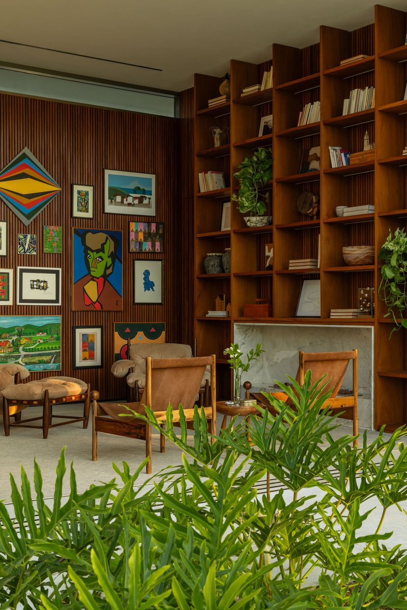 Timber bookshelf wall beside a gallery of framed artworks with potted palms in foreground