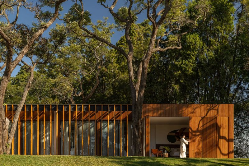 Timber facade with vertical slats and a recessed opening where a figure stands in shadow