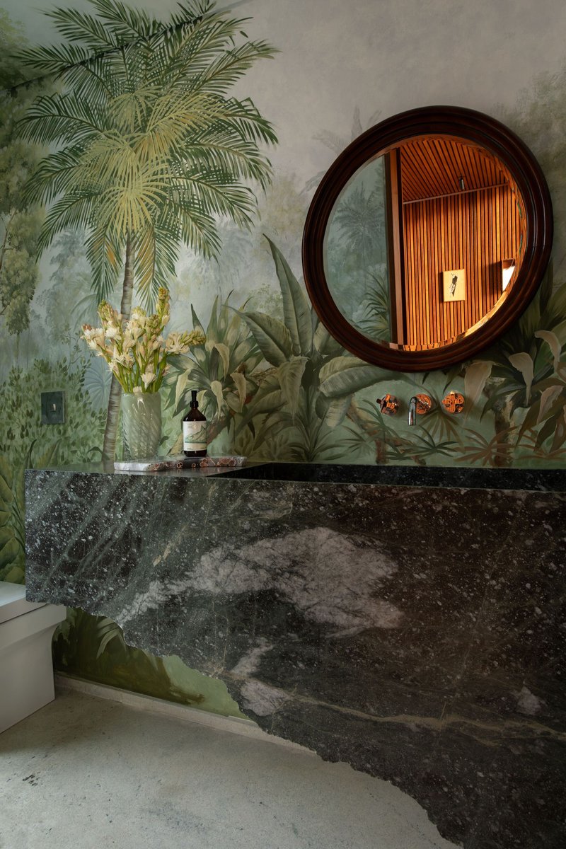 Bathroom vanity with dark stone countertop and circular mirror reflecting timber slats against botanical wallpaper
