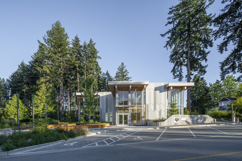 Street view of the vertical metal cladding facade with tall conifers framing the entrance