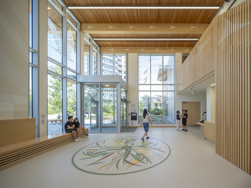 Double-height entrance lobby with exposed timber beams and a botanical floor medallion with visitors passing through