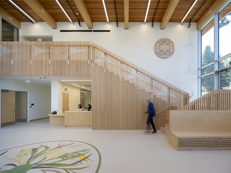 Interior lobby with vertical timber slat screen wrapping the stair and a person walking past the reception desk
