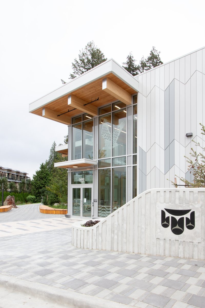 Entry facade with projecting timber soffit and chevron-patterned metal cladding under an overcast sky