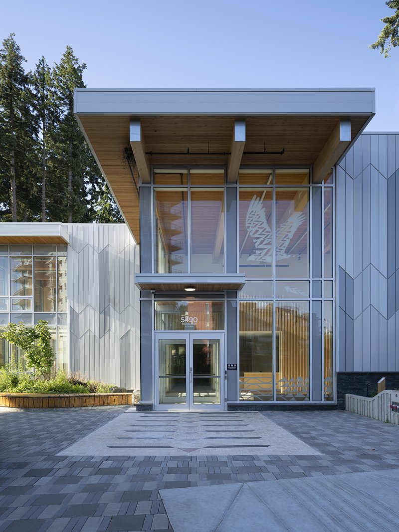 Front entrance with full-height glazing beneath the cantilevered timber soffit in afternoon light