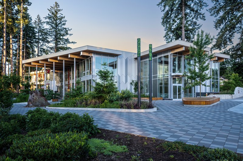 Two-story glass and metal facade with planted beds and paver courtyard at dusk