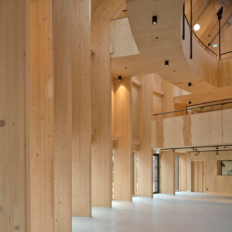 Double-height interior space showing laminated timber columns, exposed beams and mezzanine balustrade with glass railing