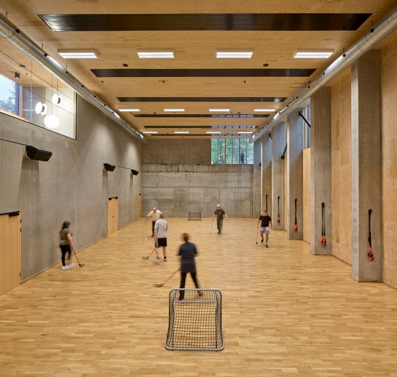 Indoor sports hall with board-marked concrete walls, timber ceiling beams and players in motion blur