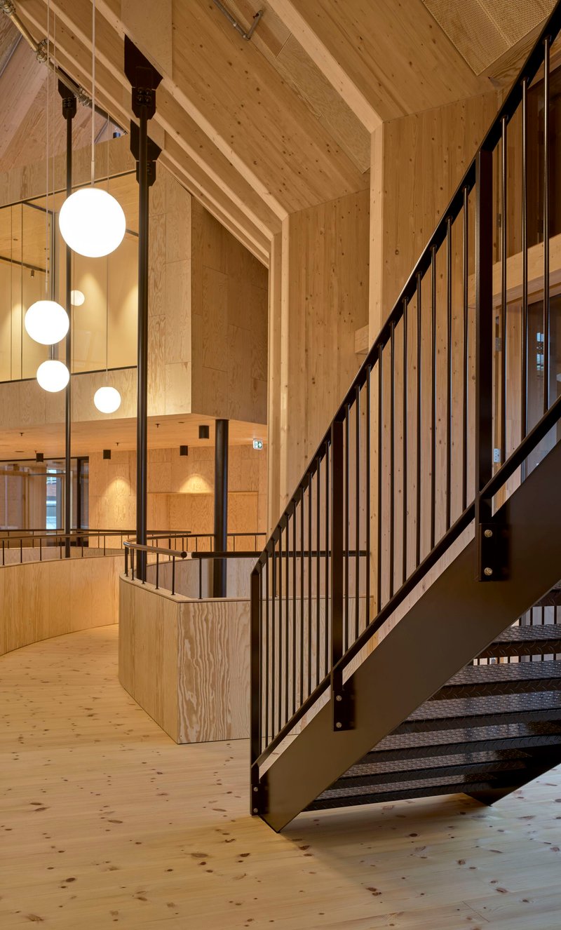 Metal staircase with vertical balusters and globe pendant lights in a timber-lined atrium