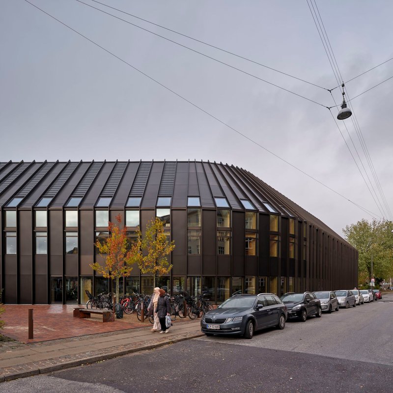 Street view of ribbed metal roof and facade with parked bicycles under autumn trees