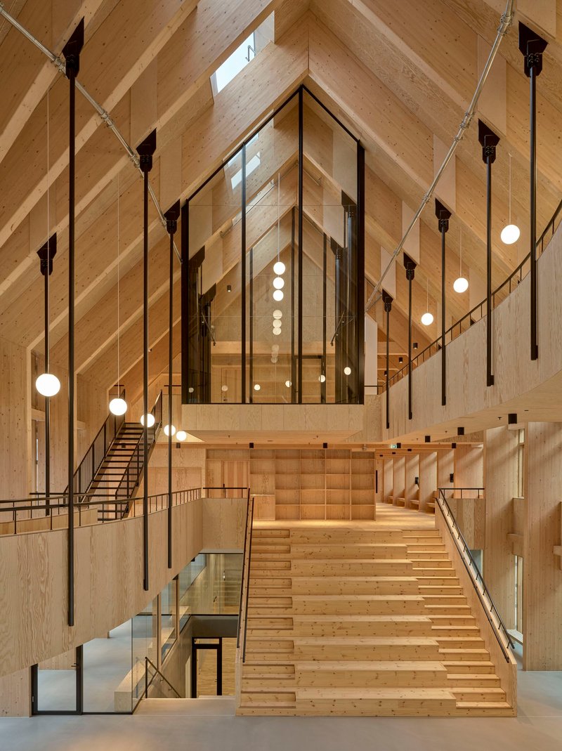 View up the stepped timber seating amphitheatre beneath diagonal laminated wood beams and pendant lighting