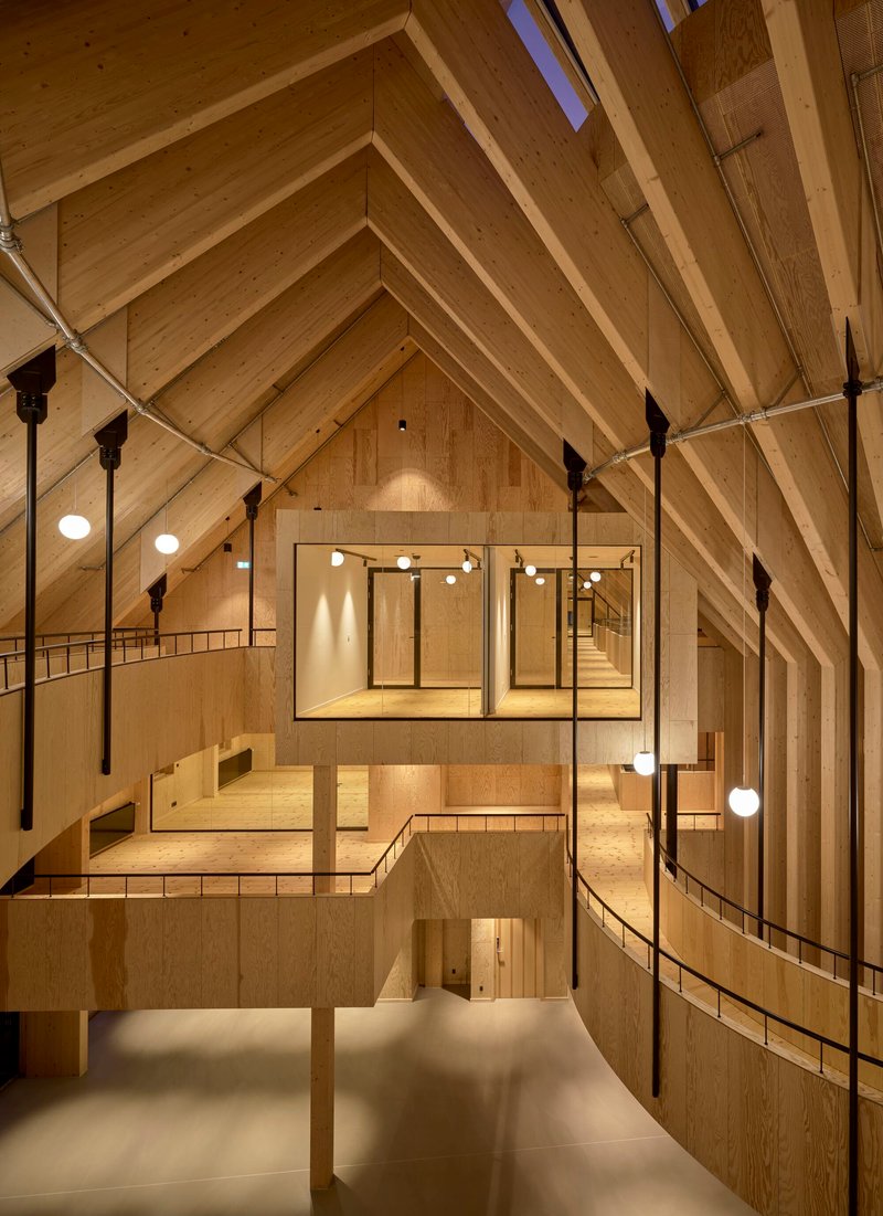 Interior view of the timber-clad volume showing exposed rafters, layered mezzanines and suspended globe pendants