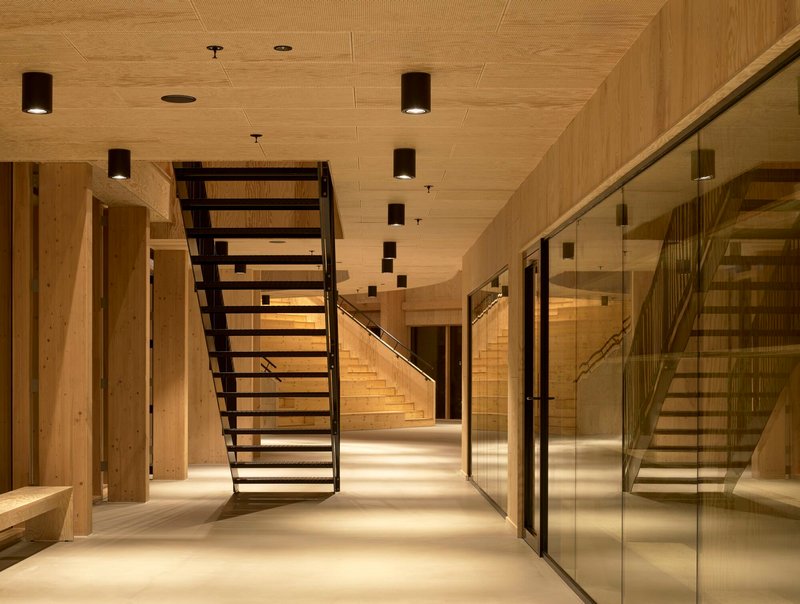 Steel staircase with open treads ascending through timber-clad corridor with glass-paneled walls