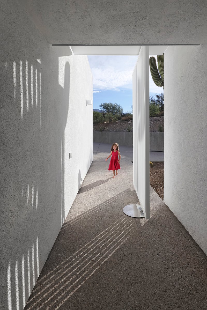 Entry corridor with patterned shadows from perforated screen and child standing in distant courtyard