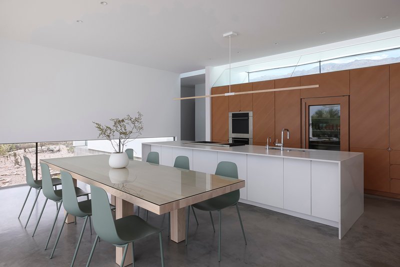 Kitchen and dining area with white island, sage chairs, and walnut-toned cabinetry wall