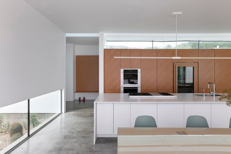 Kitchen island with polished white countertop and linear pendant light above clerestory windows