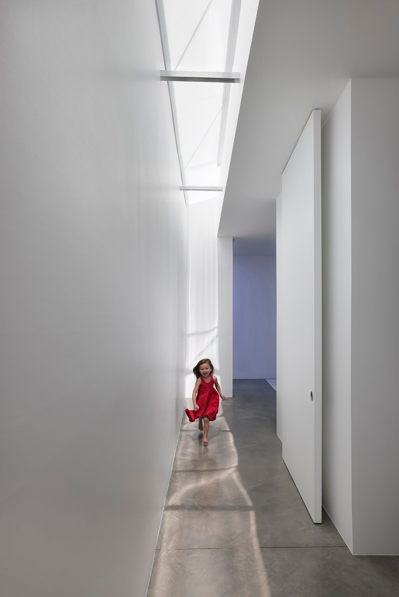 White corridor with rectangular skylights and a child walking through sunlight patches