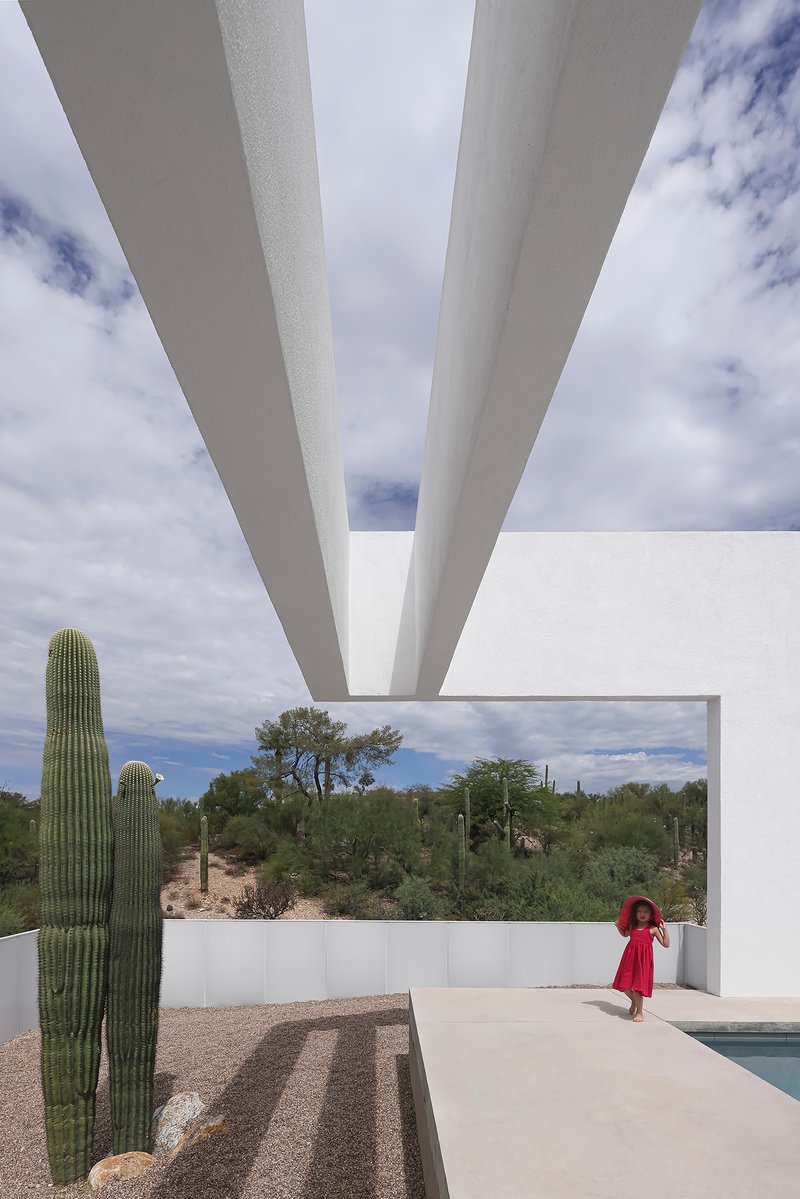 View beneath tapered white concrete roof beams overlooking the pool terrace and desert beyond