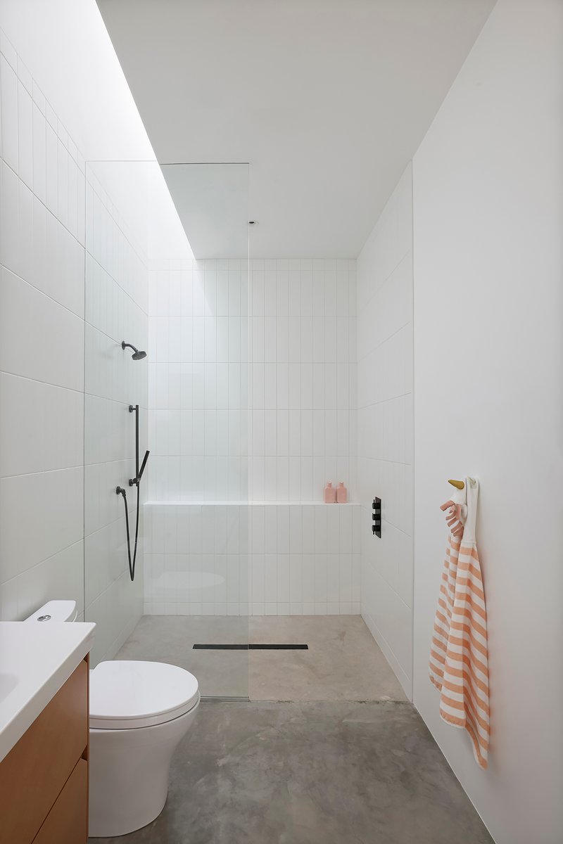 White tiled wet room with skylight, black shower fixtures, and polished concrete floor