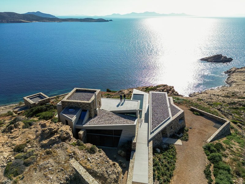 Overhead view showing the angular stone-clad volumes and white rooftops on a promontory facing open sea