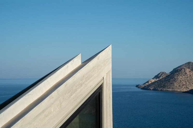 Angular concrete roof planes with a glazed corner overlooking the blue sea and distant rocky island