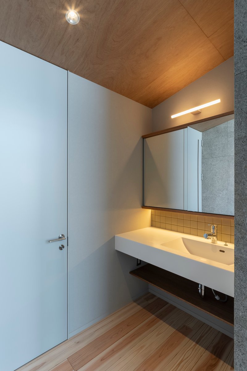 Bathroom vanity with cantilevered counter, backlit mirror and angled timber ceiling